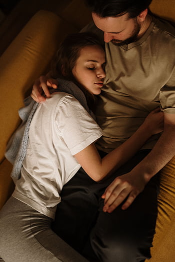 A young couple lovingly embracing on a warm-toned sofa, creating a cozy and intimate atmosphere. HD phone wallpaper