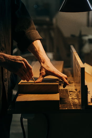 A craftsman skillfully sanding a wooden plank in a well-lit workshop. HD phone wallpaper