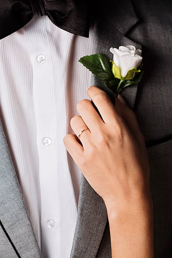Close-up of a groom's suit and boutonniere with a delicate hand touch, symbolizing elegance and romance. HD phone wallpaper