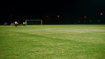 View of a soccer field at night with players and goalposts under floodlights. HD wallpaper