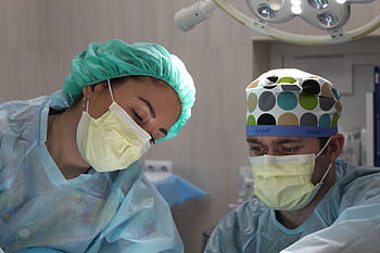 Surgeons wearing masks and scrubs conduct an operation in a hospital setting. HD wallpaper