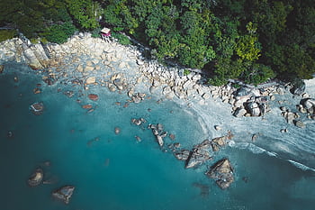 Stunning aerial shot of a rocky seashore with turquoise waters and dense forests. Perfect for nature lovers. HD wallpaper