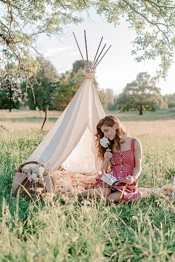 A woman in a polka dot dress enjoys a book and flower in a tranquil park setting with a tent. HD phone wallpaper
