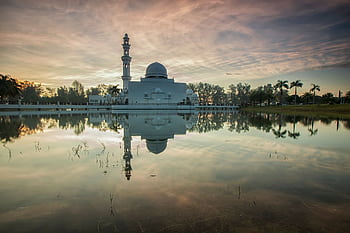 Peaceful view of a mosque reflecting in the calm waters at sunset, creating a serene landscape in Malaysia. HD wallpaper