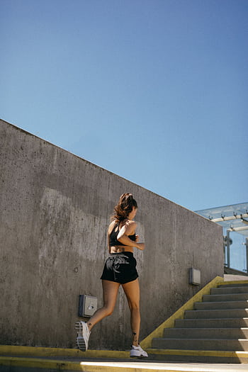 Fit woman running up outdoor stairs in sunny weather, showcasing athleticism and health. HD phone wallpaper