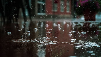 Close-up of raindrops splashing into a puddle, capturing reflections and textures in an outdoor urban setting. HD wallpaper