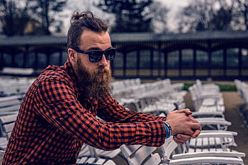 Bearded man in checkered shirt and sunglasses sitting outdoors, exuding a hipster vibe. HD wallpaper