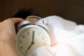 A close-up of a hand reaching for a ringing alarm clock, symbolizing waking up in the morning. HD wallpaper