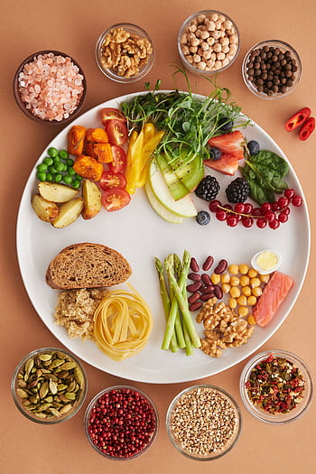 A vibrant assortment of healthy foods on a plate, showcasing a balanced diet with fruits, vegetables, nuts, and grains. HD phone wallpaper