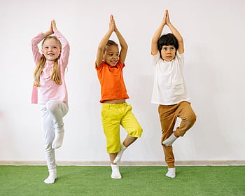 Three diverse children practicing yoga indoors, showcasing joy and balance. HD wallpaper