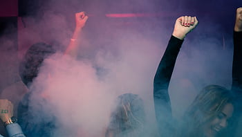 Crowd of people dancing energetically in a foggy nightclub with raised hands. HD wallpaper