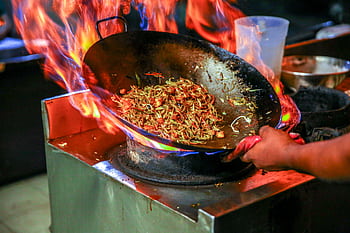 Vibrant close-up of chef cooking noodles in a flaming wok inside a restaurant kitchen. HD wallpaper