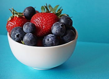 A vibrant mix of fresh strawberries and blueberries in a white bowl on a blue background. HD wallpaper