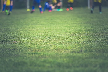 A vibrant grass field with blurred soccer players in the background during the day. HD wallpaper