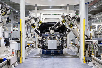 High-tech robots assembling a car in a modern factory setting, showcasing automation. HD wallpaper