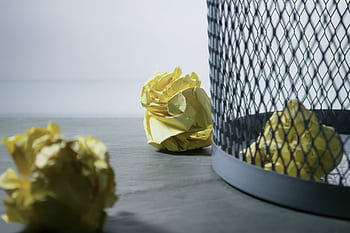 Close-up of crumpled yellow paper around a mesh trash bin, symbolizing rejected ideas or recycling. HD wallpaper