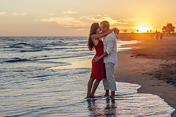 A couple in love embraces at the seaside during a vibrant sunset. HD wallpaper