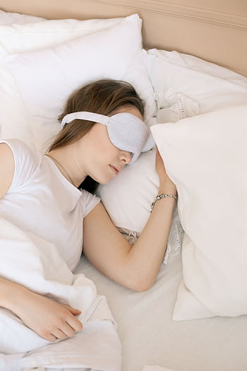 A serene scene of a woman sleeping with a white sleep mask in a cozy bed. HD phone wallpaper
