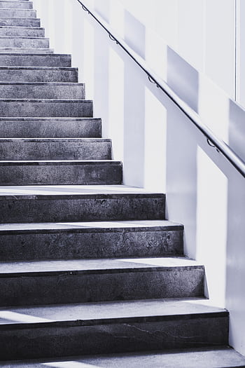 A contemporary concrete staircase with sleek steel railing and natural light casting shadows. HD phone wallpaper