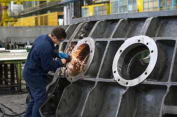 A worker in protective gear grinding metal, creating sparks in a factory setting. HD wallpaper