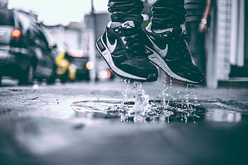 Black sneakers splashing water in city street, capturing youthful energy and urban lifestyle. HD wallpaper