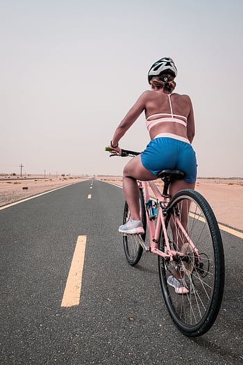 A woman in active wear enjoys cycling along a deserted road in Dubai. HD phone wallpaper
