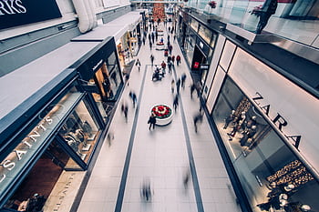 A vibrant scene capturing a busy shopping mall with modern stores and diverse shoppers on the move. HD wallpaper