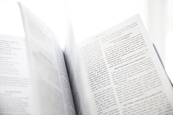 Close-up of an open book with visible text and turning pages in natural light. HD wallpaper