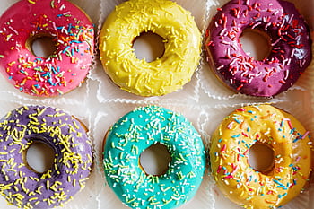 Assorted colorful glazed donuts with sprinkles arranged in a flat lay. HD wallpaper