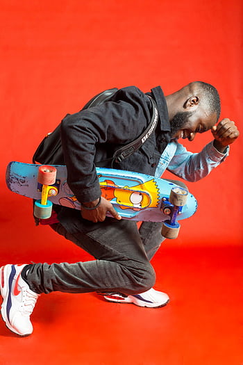 Stylish young man posing with a skateboard against a vibrant red background. HD phone wallpaper