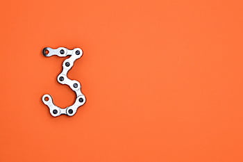 A bicycle chain forms the number three against a vibrant orange backdrop, offering ample copyspace. HD wallpaper