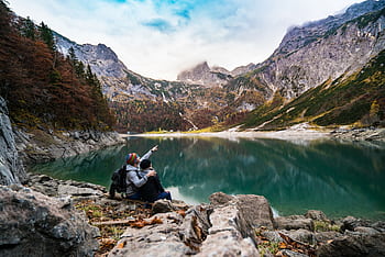 A couple enjoys a scenic view of Hallstatt Lake surrounded by mountains and fores. HD wallpaper