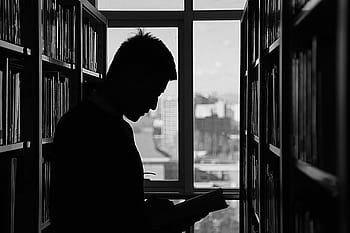 A moody silhouette of a man reading in a library, capturing solitude and contemplation. HD wallpaper