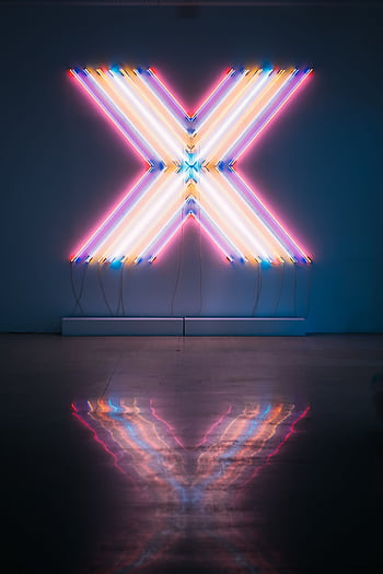 Vibrant neon X sign with colorful reflections on a dark floor background. HD phone wallpaper