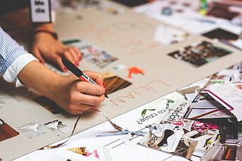 Close-up of a person writing and crafting at a cluttered desk workspace. HD wallpaper