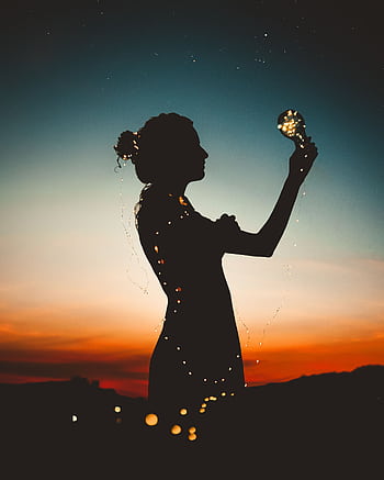 Artistic silhouette of a woman wrapped in fairy lights during a vibrant sunset. HD phone wallpaper