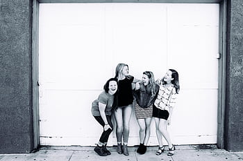 Four young women laughing together in front of an urban door, showcasing friendship and happiness. HD wallpaper