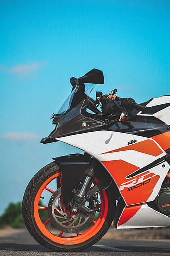Detailed view of a sporty orange and black motorcycle under clear blue skies. HD phone wallpaper