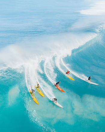Dynamic aerial capturing surfers conquering massive waves in vibrant blue Hawaiian waters. HD phone wallpaper
