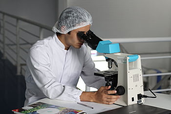 Scientist in a lab coat using a microscope to conduct research, focusing on healthcare improvements. HD wallpaper