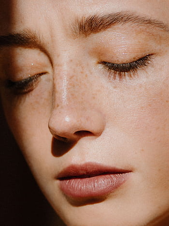 Gentle close-up portrait of a freckled woman with serene expression under sunlight. HD phone wallpaper