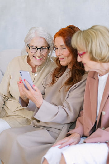 Three senior women smiling while looking at a smart indoors, enjoying technology. HD phone wallpaper