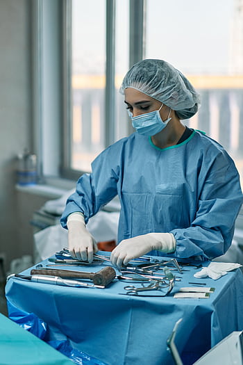 A female surgeon wearing protective gear arranges surgical instruments in a hospital operating room. HD phone wallpaper