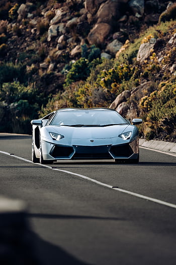 A stunning Lamborghini Aventador driving on a scenic road with rocky hillsides. HD phone wallpaper