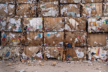 Large bales of recycled cardboard stacked outdoors, ready for processing. HD wallpaper