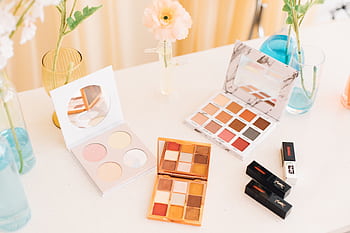 Aesthetic display of makeup palettes and lipsticks surrounded by flowers. HD wallpaper
