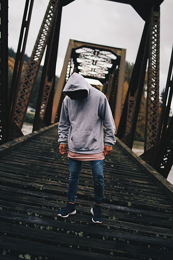 Man in hoodie on a rustic urban bridge during daylight, showcasing casual street fashion. HD phone wallpaper
