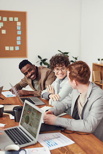 Engaged professionals collaborating during a meeting with laptops and charts on wooden table. HD phone wallpaper