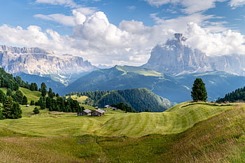 Idyllic landscape in the Dolomites, Italy with lush green fields and majestic mountains under a blue sky. HD wallpaper