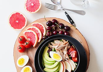 A vibrant breakfast flat lay featuring a mix of fruits, avocado, eggs, tomatoes, and sliced meats on a wooden platter. HD wallpaper